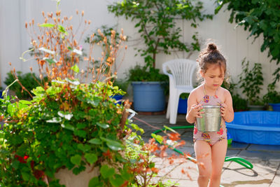 Cute young girl watering plants with a bucket on a summer day in the backyard