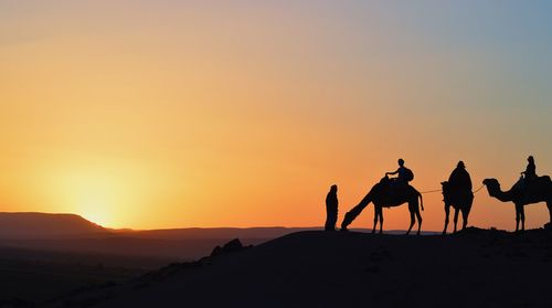 Silhouette people riding motorcycle on desert against sky during sunset