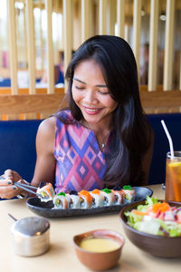 Happy young woman having sushi while sitting at restaurant