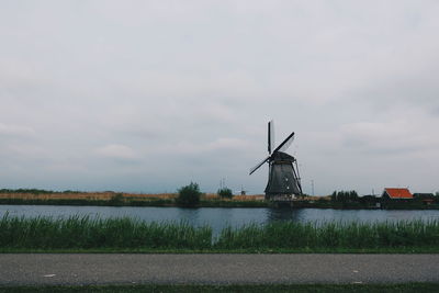 Traditional windmill by lake against sky