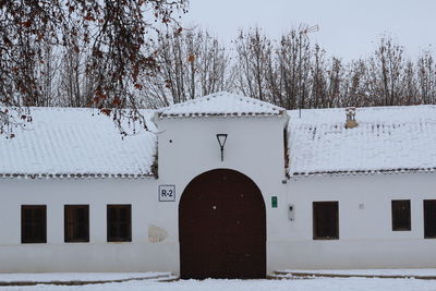 Snow covered trees by building against sky