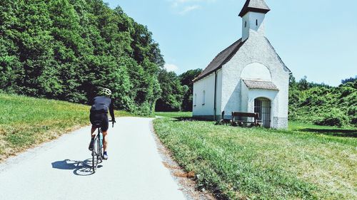 Rear view of man riding bicycle on street amidst buildings