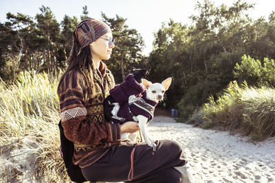 Two dogs sit on womans lap in pretty sunlight on natural beach