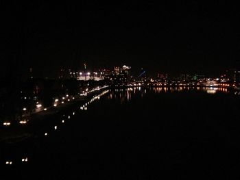 Illuminated city by river against sky at night