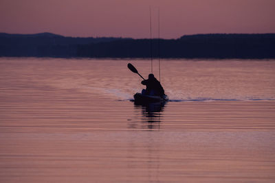 Silhouette man in boat on sea against sky during sunset