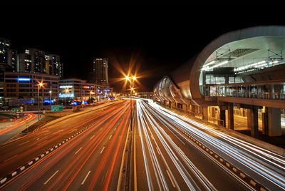 Light trails on illuminated city against sky at night