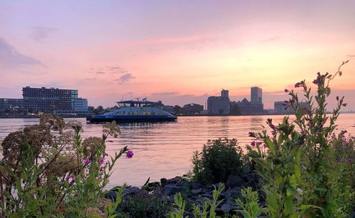 Scenic view of river by buildings against sky during sunset