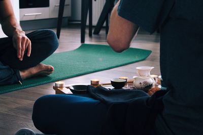 Midsection of man with friend having drink while sitting on floor at home