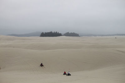 High angle view of people riding quadbikes at desert against sky