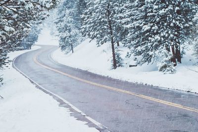 Snow covered road by trees