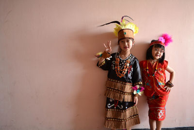 Portrait of smiling children standing against wall on traditional costume