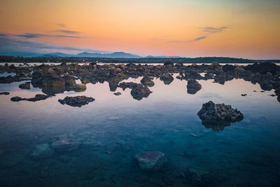 Rocks in sea against sky during sunset