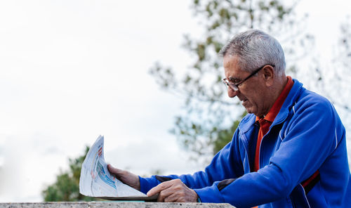 Senior man reading newspaper at park, side view