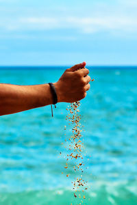 Close-up of hand holding sea against blue sky