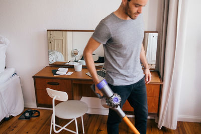 Mid adult man cleaning bedroom with vacuum cleaner