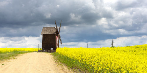 Old wooden mill in the midst of flowering rape with storm clouds