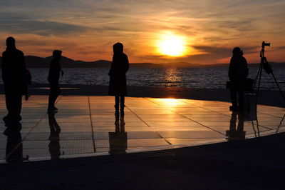 Silhouette people standing by sea against sky during sunset