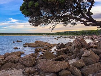 Scenic view of rocky shore against sky at sunset