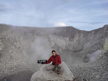 Portrait of man sitting on mountain against sky