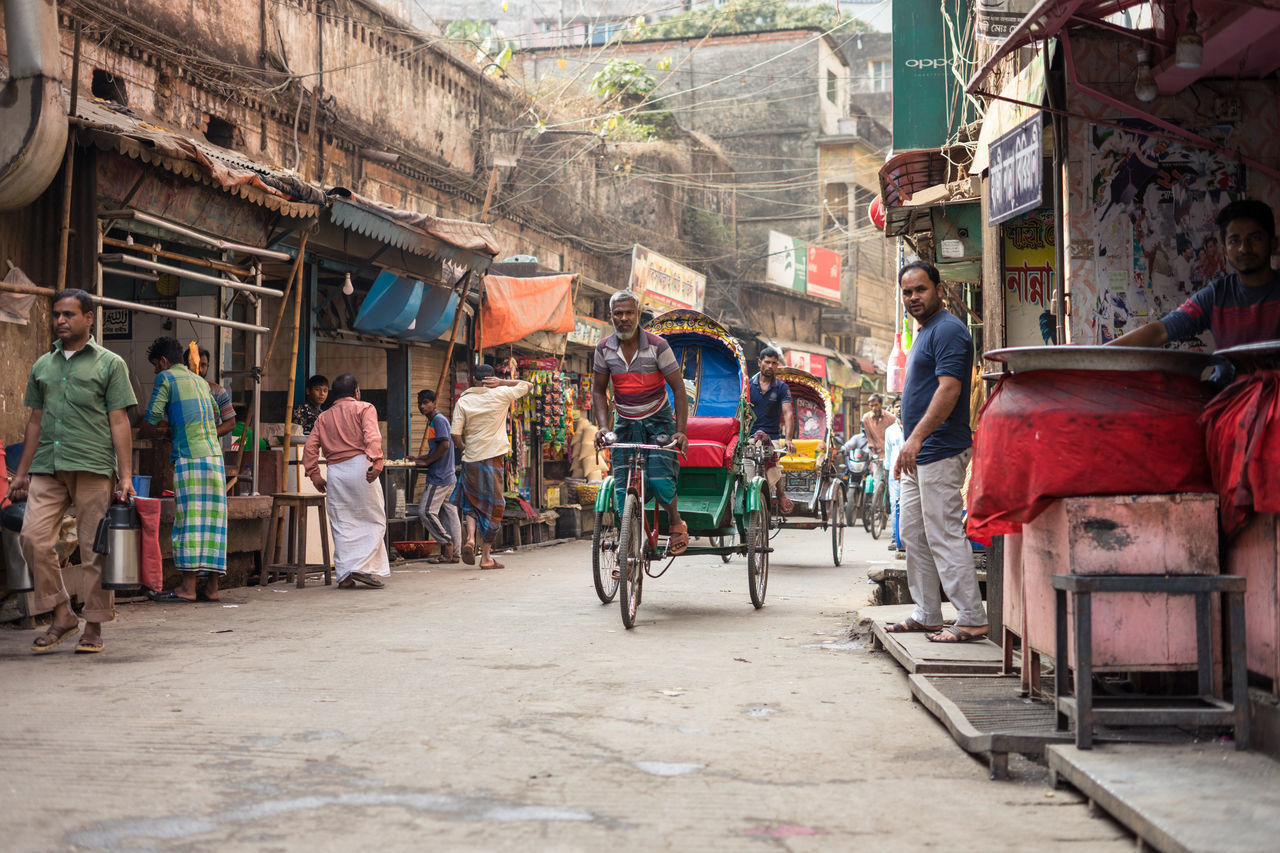 Bangladesh - january, 20 2019: traditional rickshaws with ethnic men and full sacks riding on asphalt road through market street in town