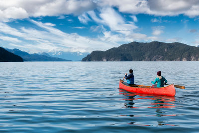 People on boat in lake against sky