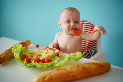 A child eats sausage with pasta and baguette