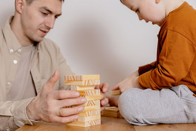 Father and son sitting together at home and playing with wooden blocks. jenga game.