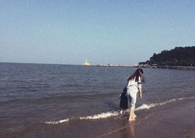 Mother with daughter walking on sea shore against clear sky