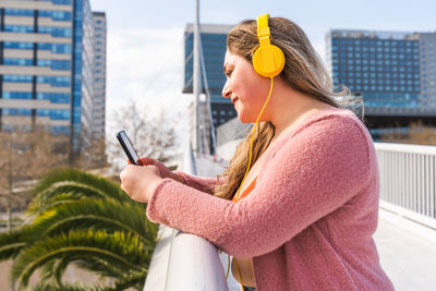 Young woman listening music against sky
