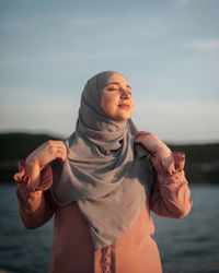 Portrait of young woman standing against sky during sunset