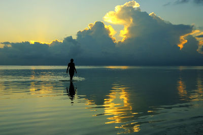 Rear view of woman standing in sea against sky during sunset