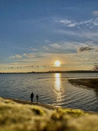 Rear view of woman walking at beach against sky during sunset
