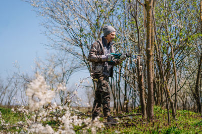 Full length of man using saw standing by tree in forest