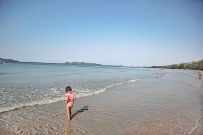 Rear view of girl on beach against clear sky