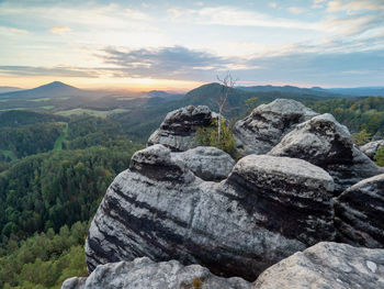 Autumn in mountains at sunset time. different trees, hill peaks, clouds and colorful sunset