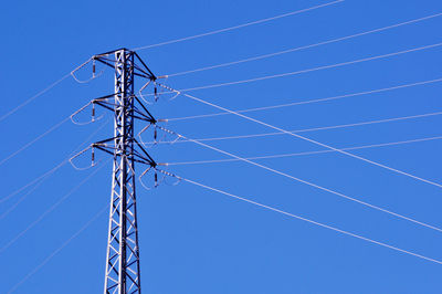 Low angle view of electricity pylon against clear blue sky