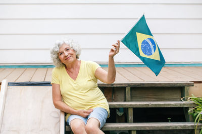 Portrait of senior woman holding brazilian flag sitting on steps