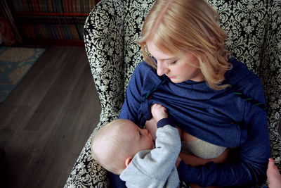 High angle view of mother breastfeeding son while sitting at home