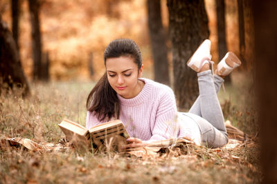 Woman reading book while lying at park during autumn