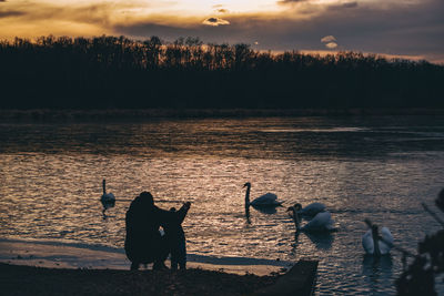 Silhouette men by lake against sky during sunset