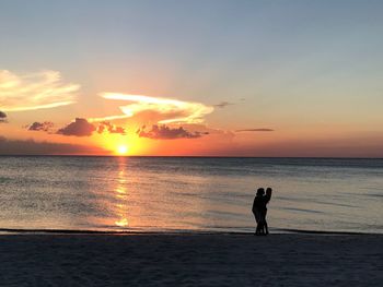 Silhouette people on beach against sky during sunset