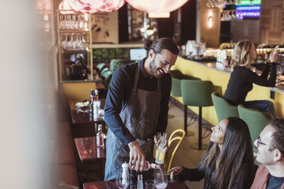 Smiling waiter pouring wine to male and female customers in bar