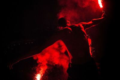 Rear view of shirtless male performer holding red distress flares