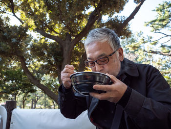 An older asian man eating noodles and soup with chopsticks