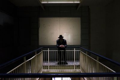 Man wearing hat standing by railing in dark building