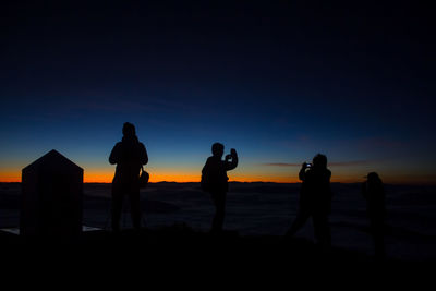Silhouette people standing on land against sky during sunset