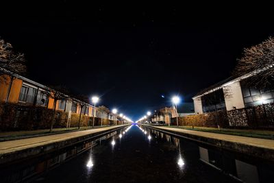 Illuminated road by canal against sky at night