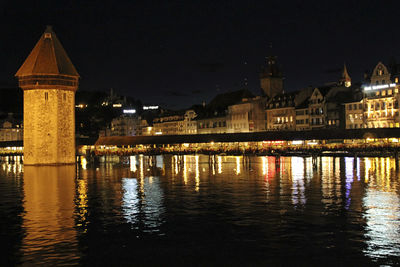 Illuminated buildings by river against sky at night