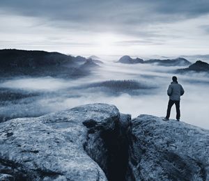 Rear view of man standing on rock against sky