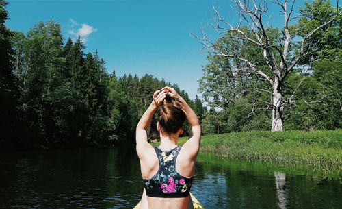 Young woman standing against lake and trees against sky